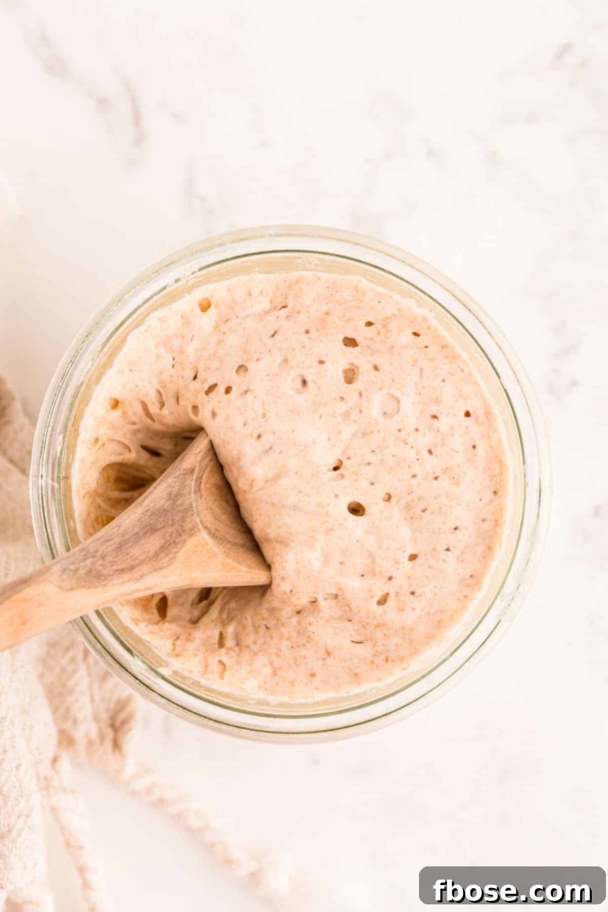 Building a Sourdough Starter 11 A wooden spoon scooping sourdough starter out of a glass jar.