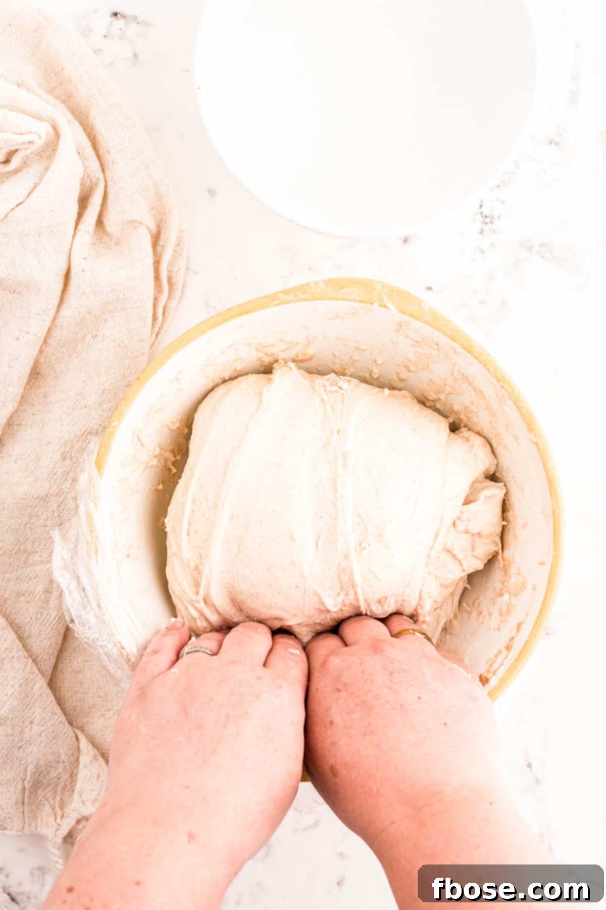 A baker's hands lifting the entire mass of sourdough dough from the bowl, stretching it upwards.