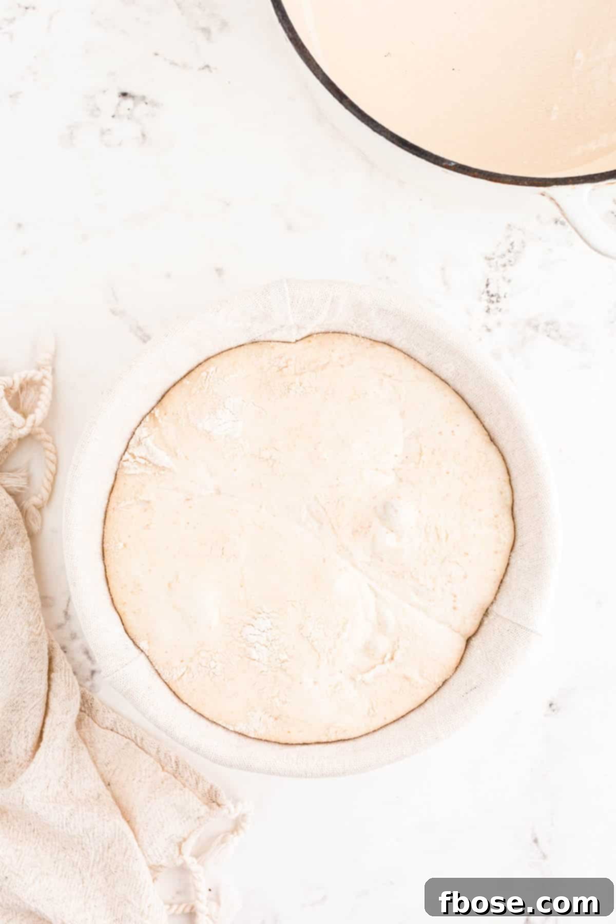 Shaped sourdough bread dough resting in a banneton, lightly dusted with rice flour and covered for cold proofing.