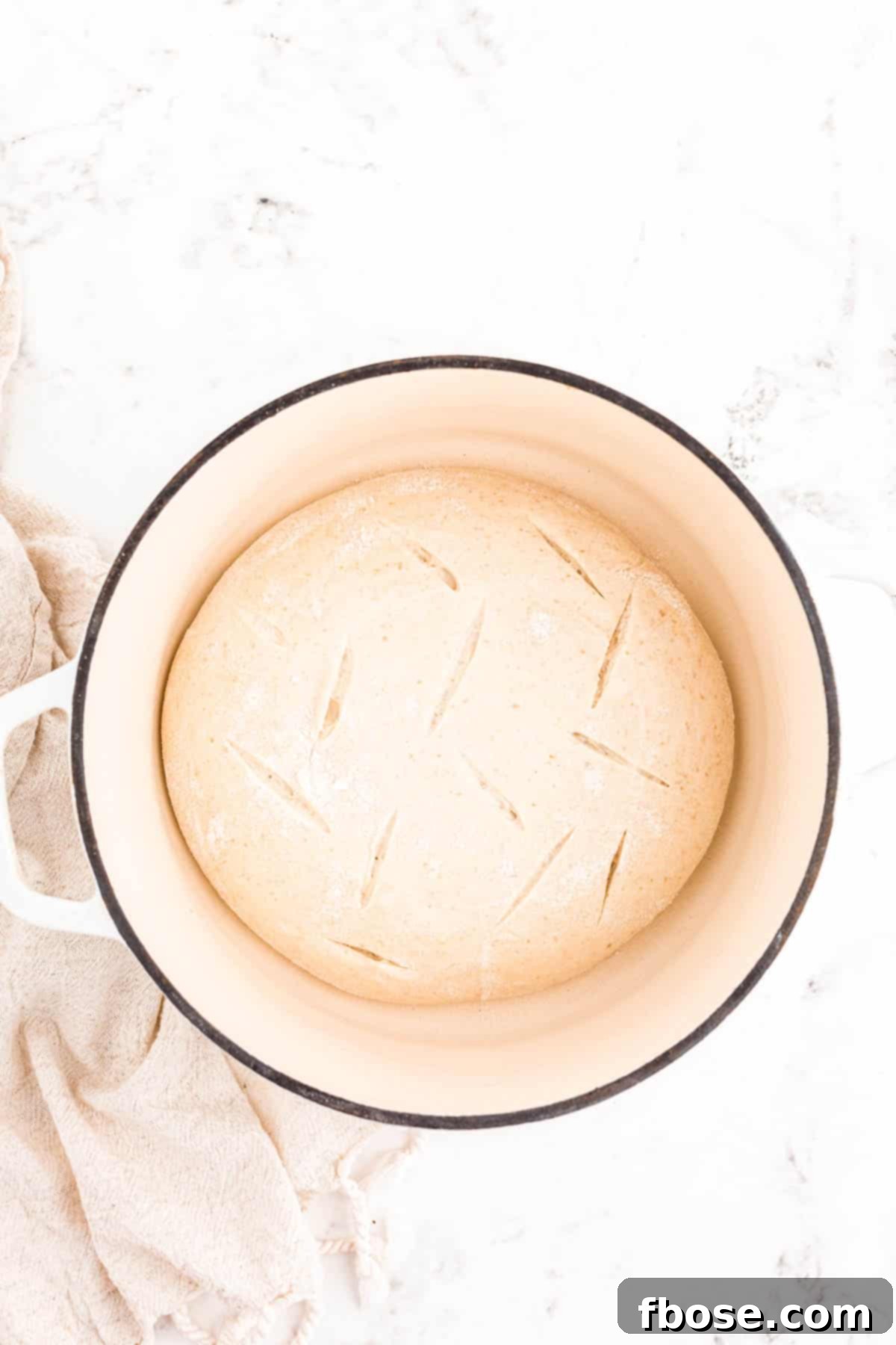 Sourdough bread dough precisely scored with a lame in a Dutch oven, poised for baking.