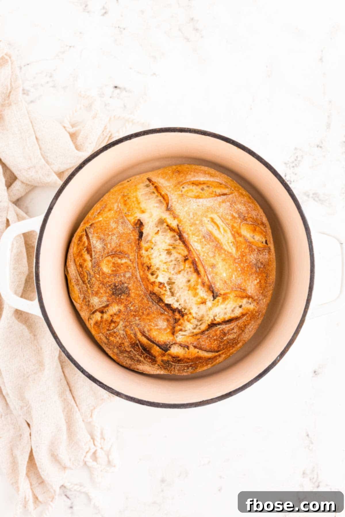 A perfectly baked, golden-brown loaf of sourdough bread resting in a Dutch oven after being removed from the oven.