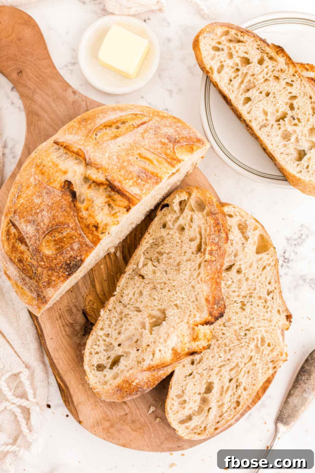 Overhead photo of a freshly baked loaf of sourdough bread on a cutting board with several slices next to it.