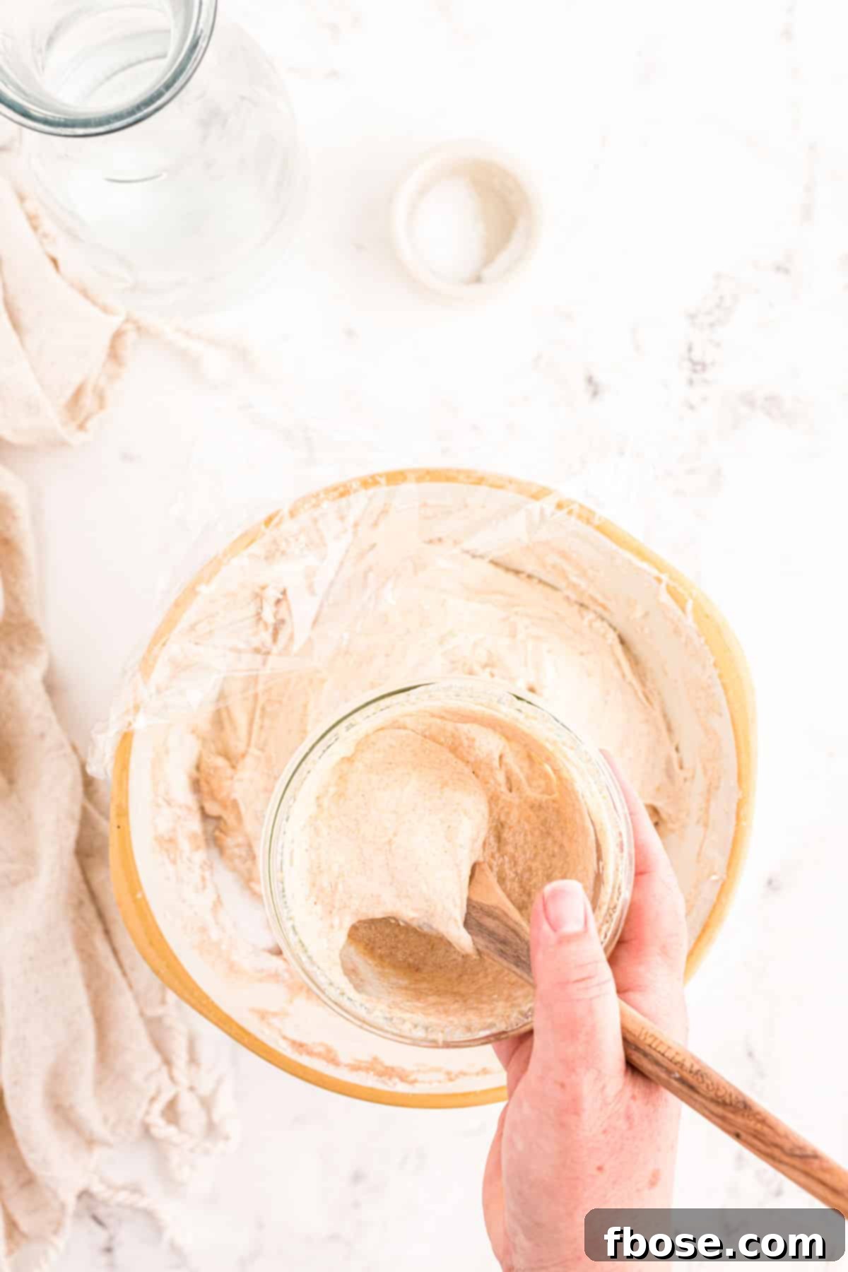 Active sourdough starter being added to the autolysed dough mixture in a bowl.