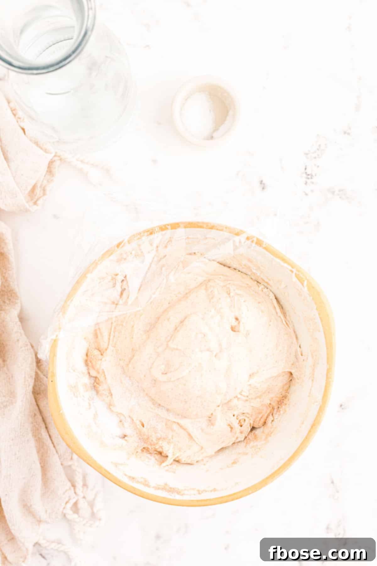 Sourdough dough, now enriched with starter and salt, resting in a bowl covered with plastic wrap.