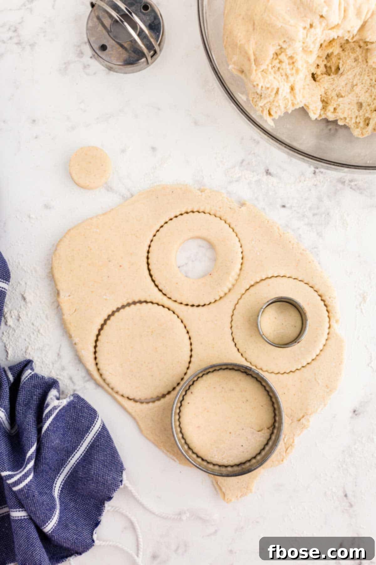 Donuts being cut out of dough with a cutter.