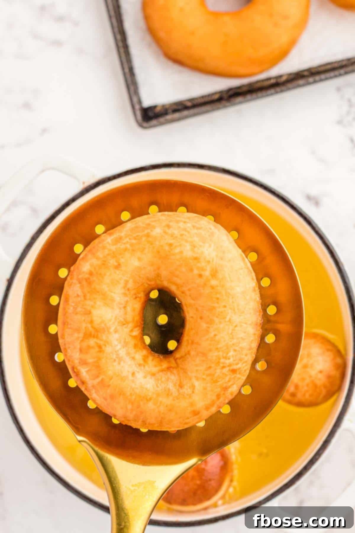 A slotted spoon lifting a fried donut out of oil pan.