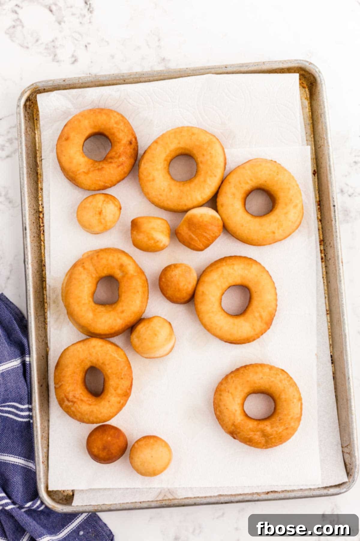 Fried donuts on a paper towel lined baking sheet.