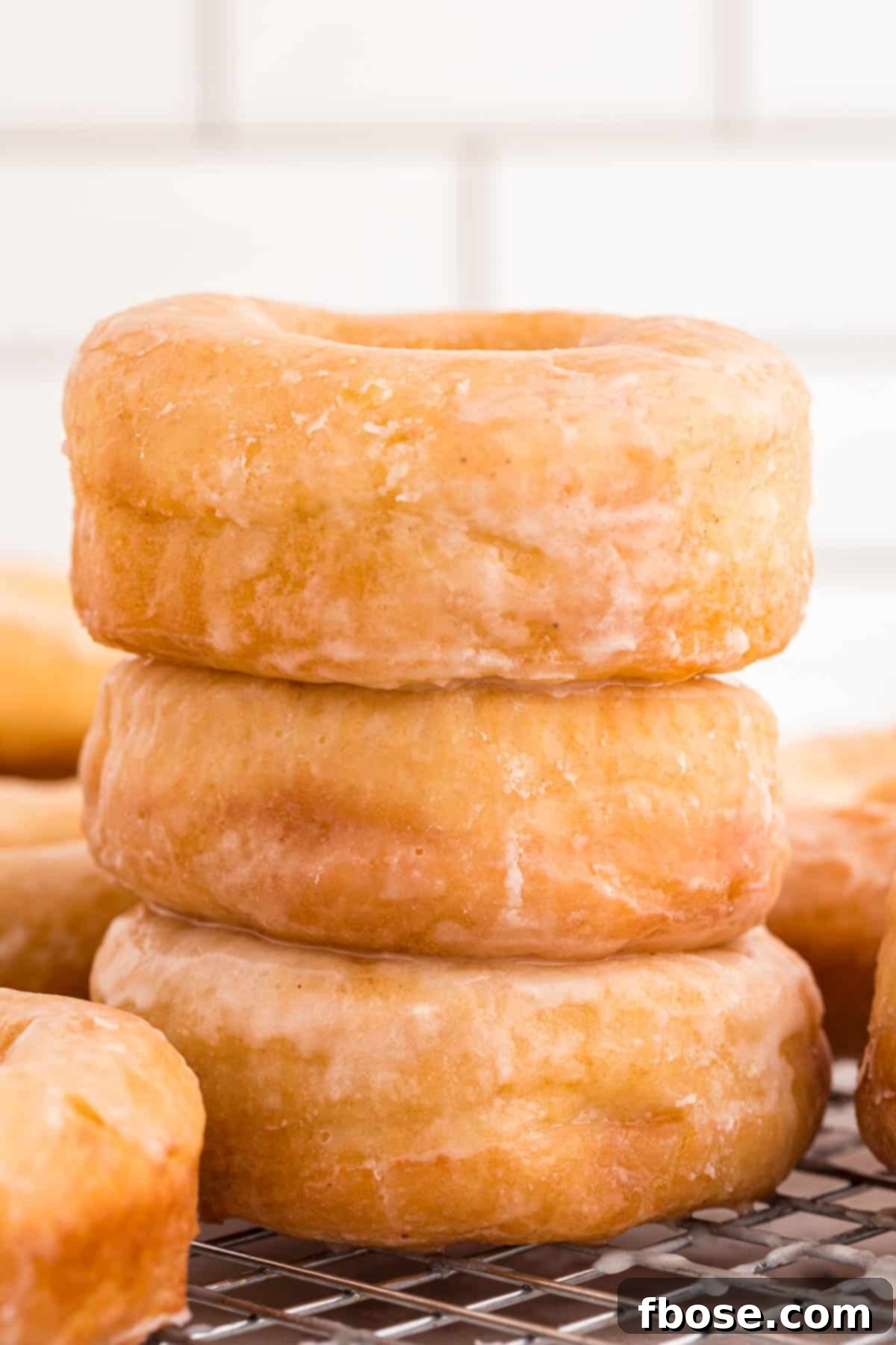 A stack of three glazed donuts on a wire rack.