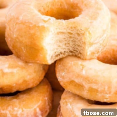 Close up photo of sourdough donuts piled on a cutting board, the top one is missing a bite.