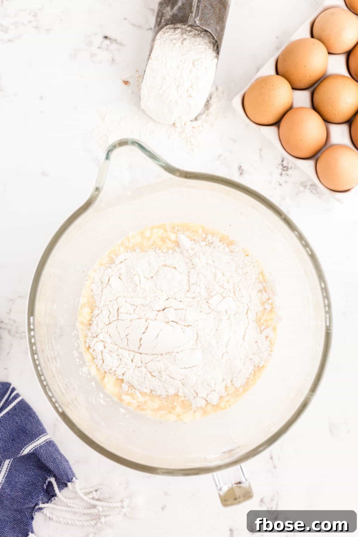 Flour being added to a glass mixing bowl to make donut dough.