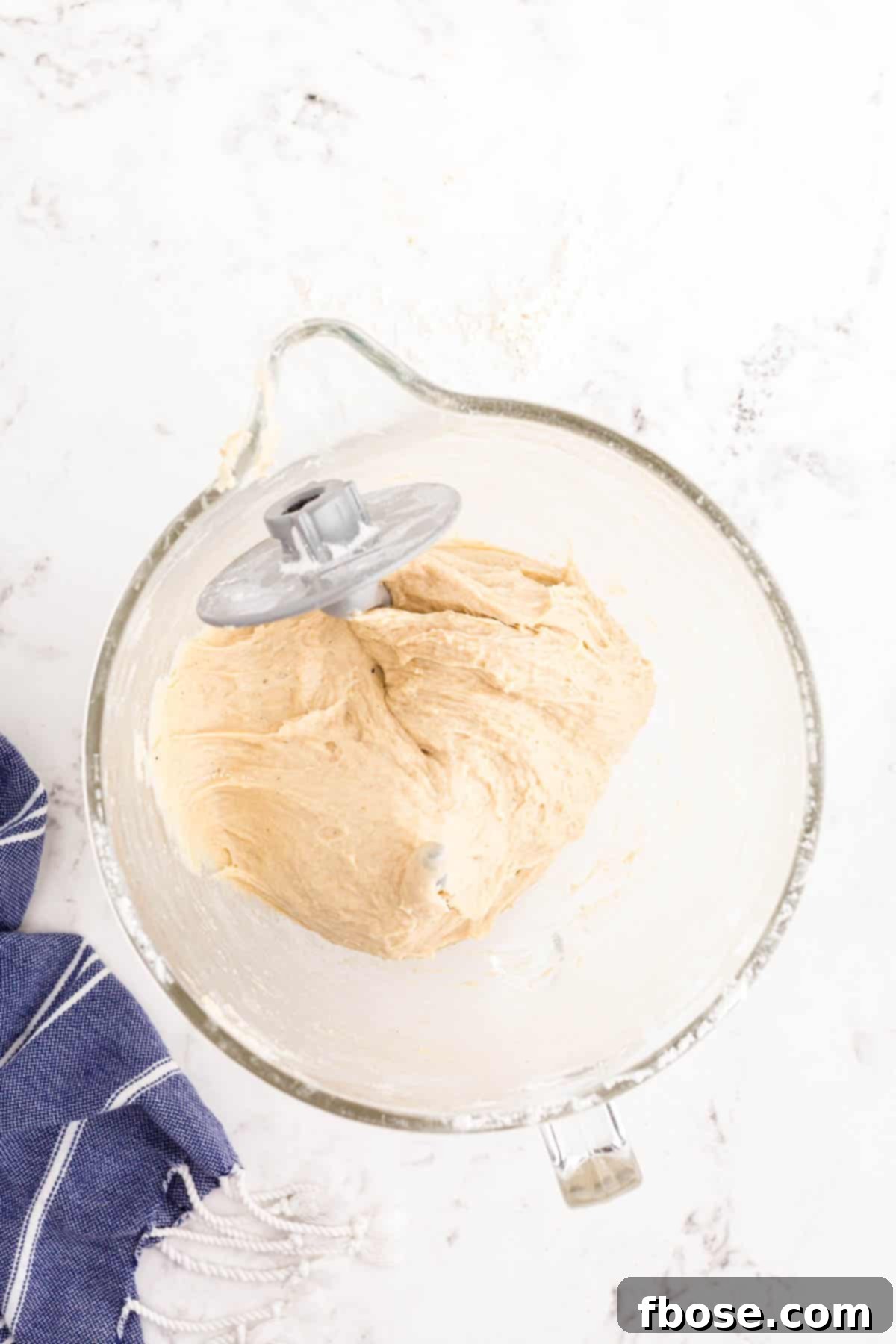 A glass mixing bowl with dough and a dough hook in it.