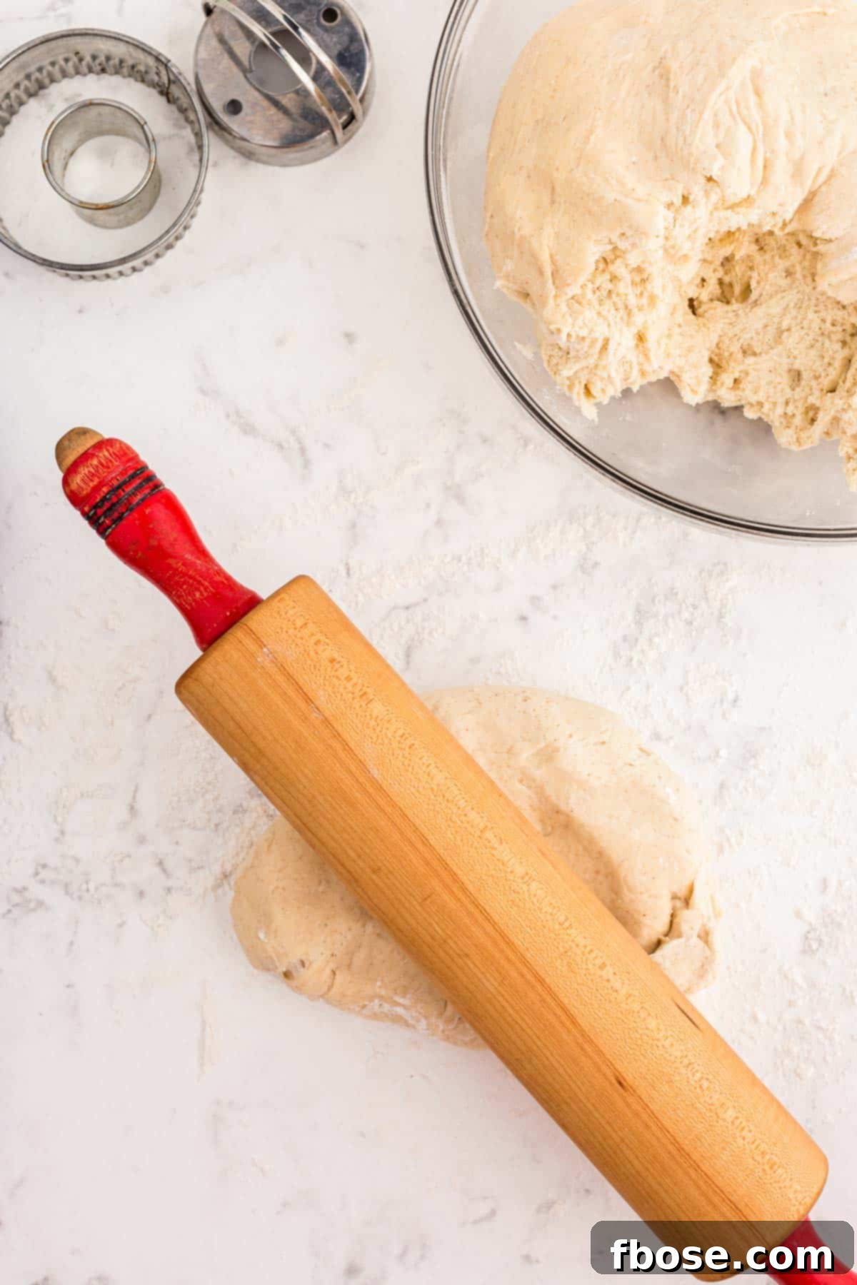 Donut dough being rolled out with a rolling pin.
