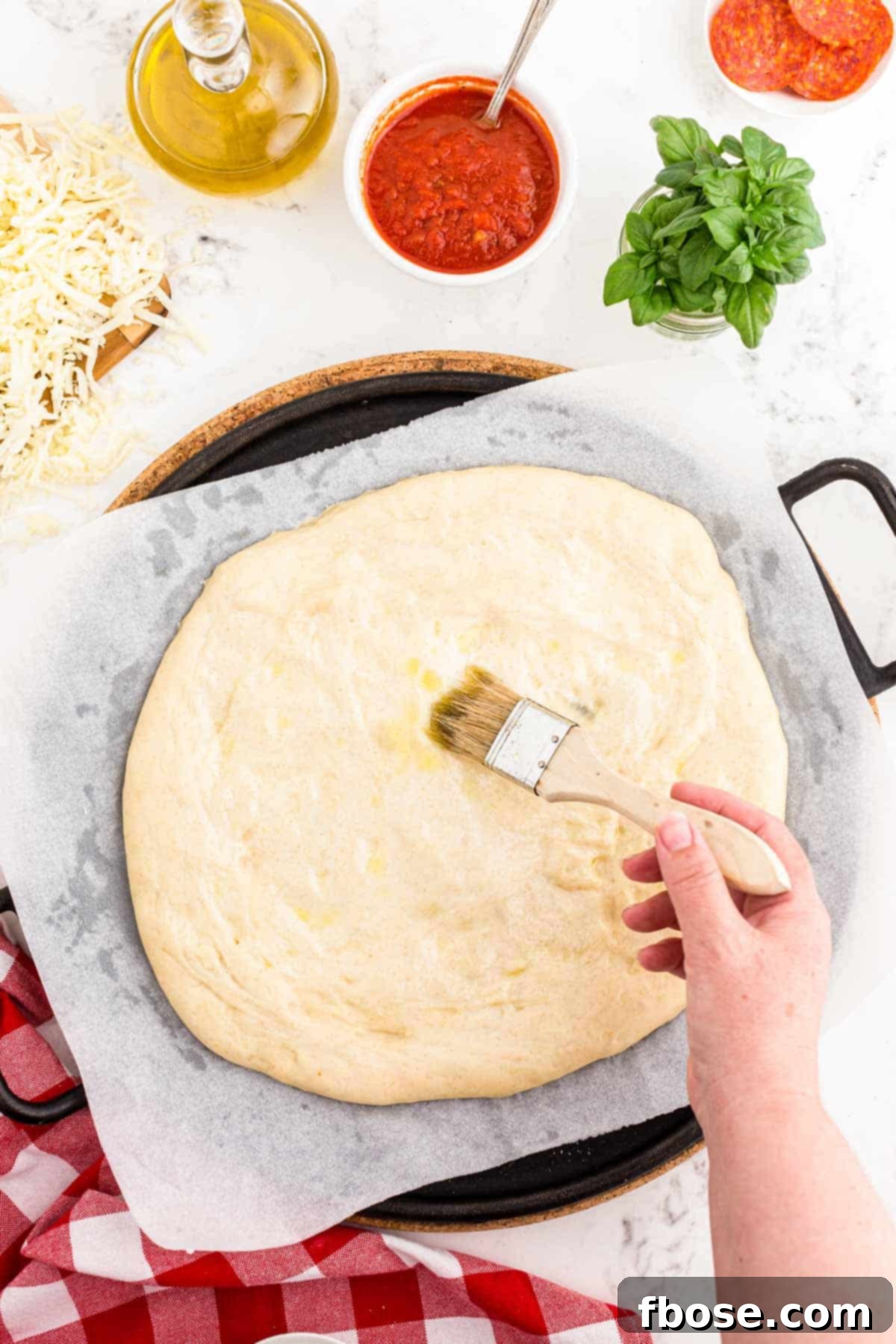 Perfect Sourdough Pizza Dough 15 Sourdough pizza crust being gently shaped and brushed with olive oil on parchment paper, laid on a pizza stone, ready for its final proof.