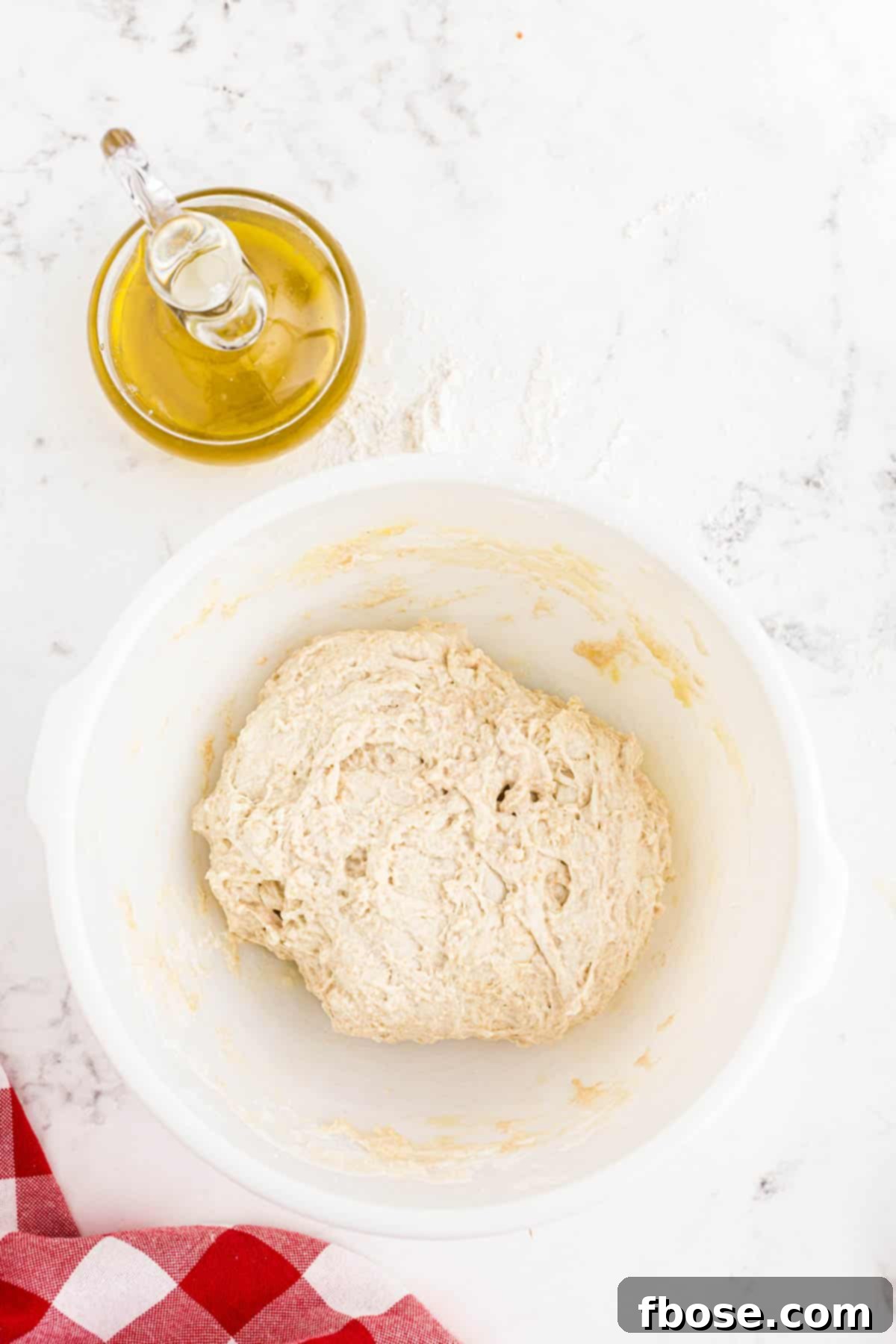 Perfect Sourdough Pizza Dough 8 A smooth, round sourdough pizza dough resting in a white mixing bowl, covered and ready for its first fermentation period.