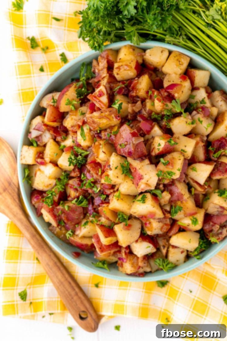 Overhead photo of German potato salad in a teal bowl on a yellow checkered napkin.