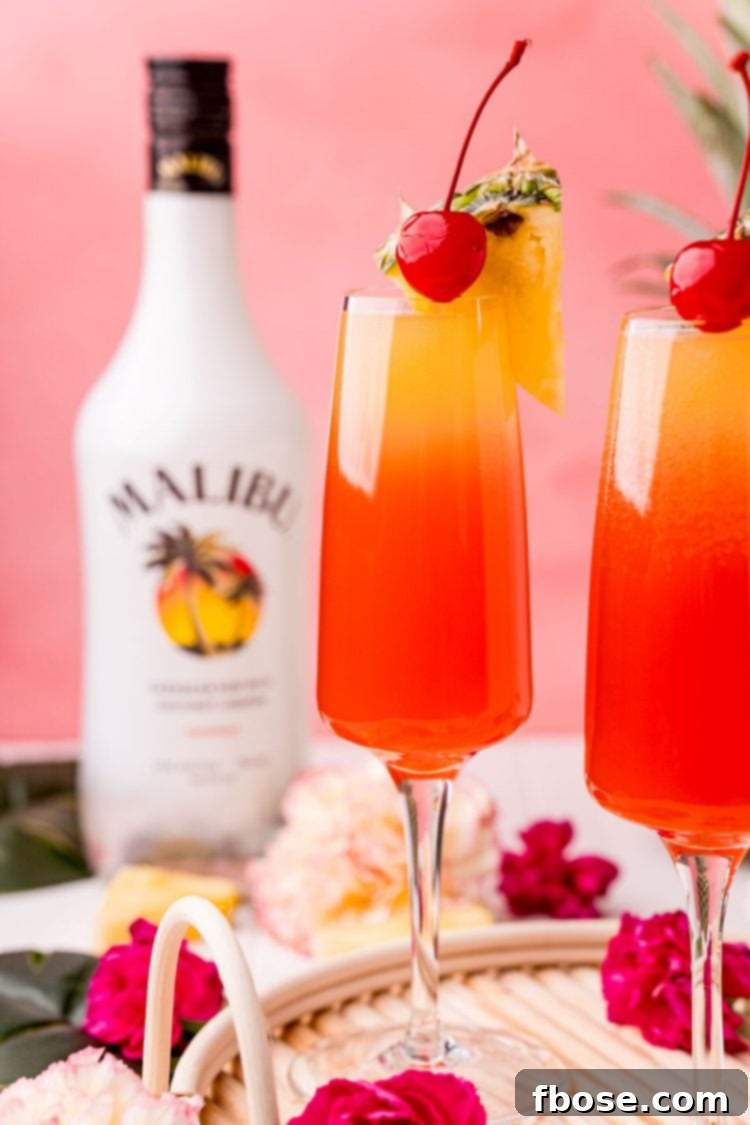 Close up photo of two Hawaiian Mimosas in champagne flutes garnished with pineapple wedges and cherries.