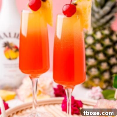 Close up photo of two Hawaiian Mimosas in champagne flutes garnished with pineapple wedges and cherries.