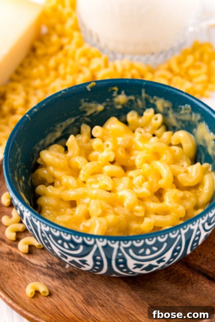 Close-up photo of mac and cheese in a teal mug resting on a rustic wooden plate, ready to be served.