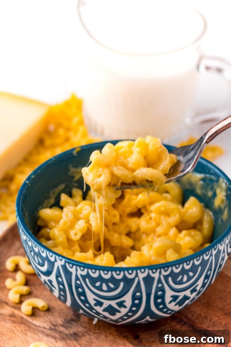 A fork scooping a generous bite of creamy mac and cheese out of a bright blue mug, highlighting the texture.