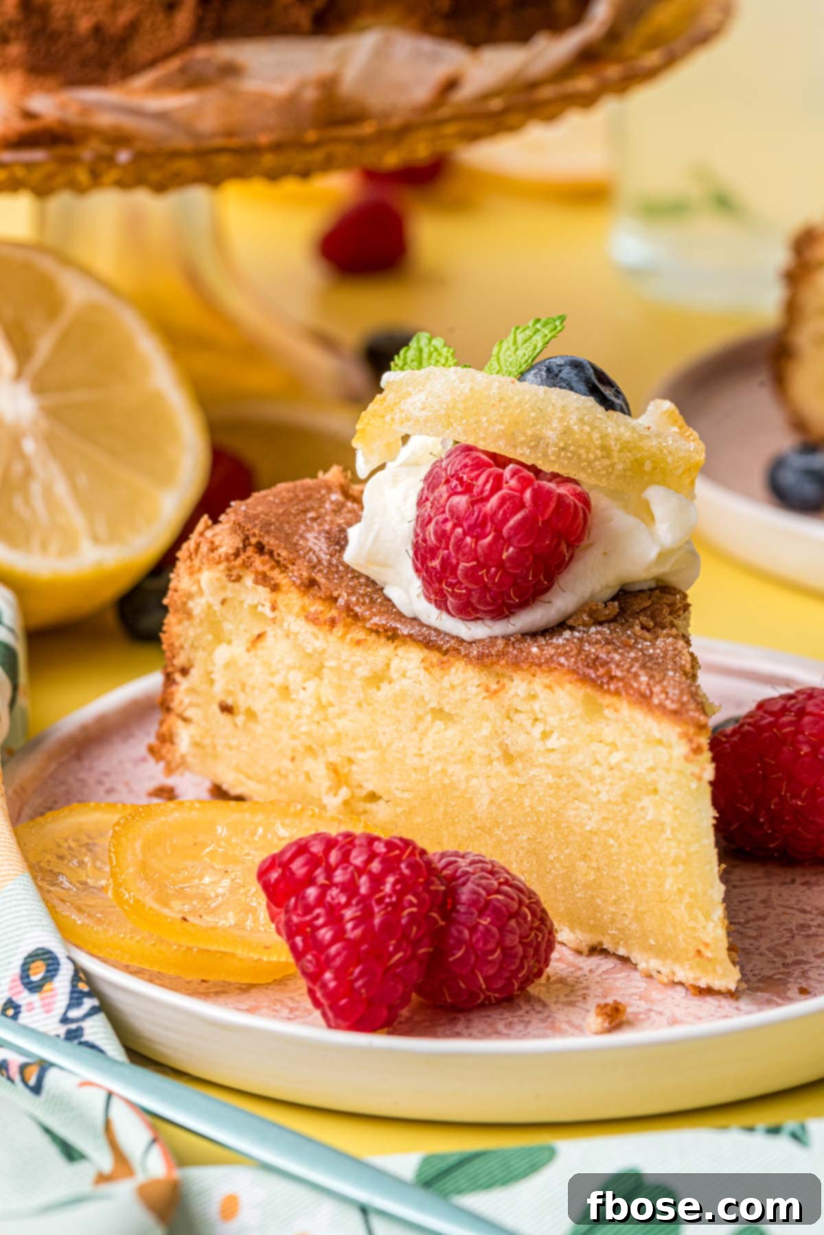 A beautifully sliced lemon olive oil cake resting on a delicate pink plate, set against a cheerful yellow background. The golden-brown crust and moist interior are visible, hinting at its deliciousness.