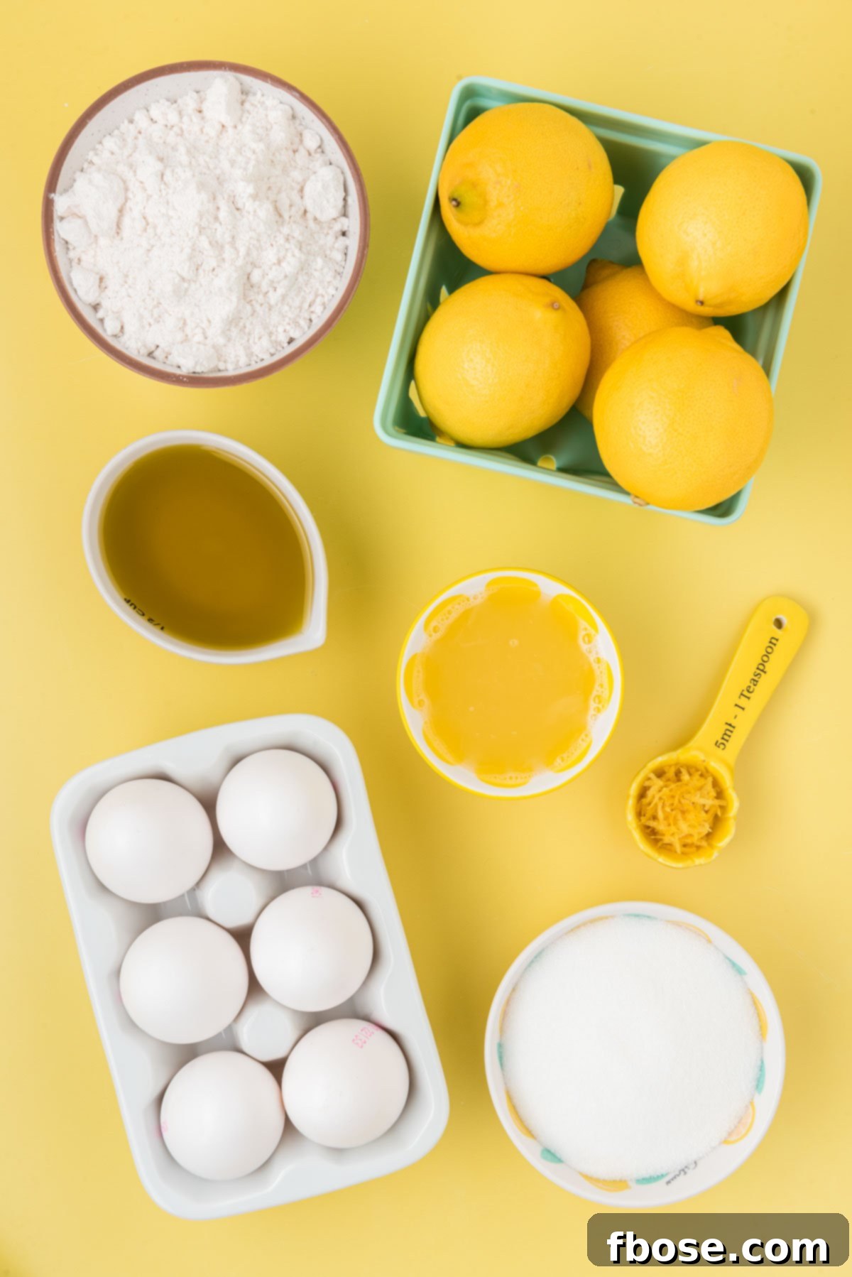 A collection of fresh ingredients neatly arranged on a bright yellow surface, ready to be transformed into a delicious lemon olive oil cake. Lemons, olive oil, eggs, and flour are prominently displayed.