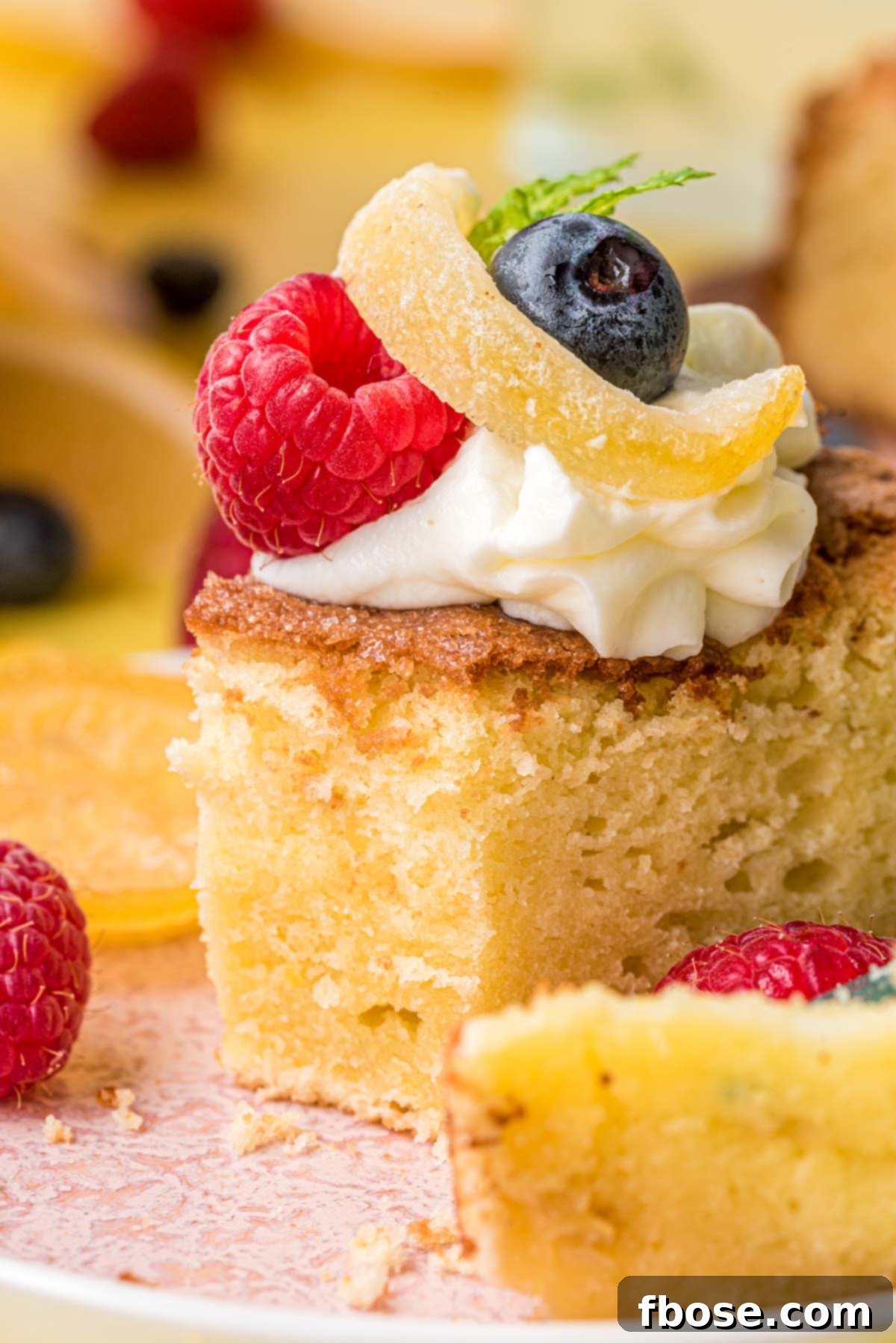 A luscious slice of lemon olive oil cake on a white plate, elegantly topped with creamy whipped cream and a scattering of fresh berries. It looks absolutely irresistible.