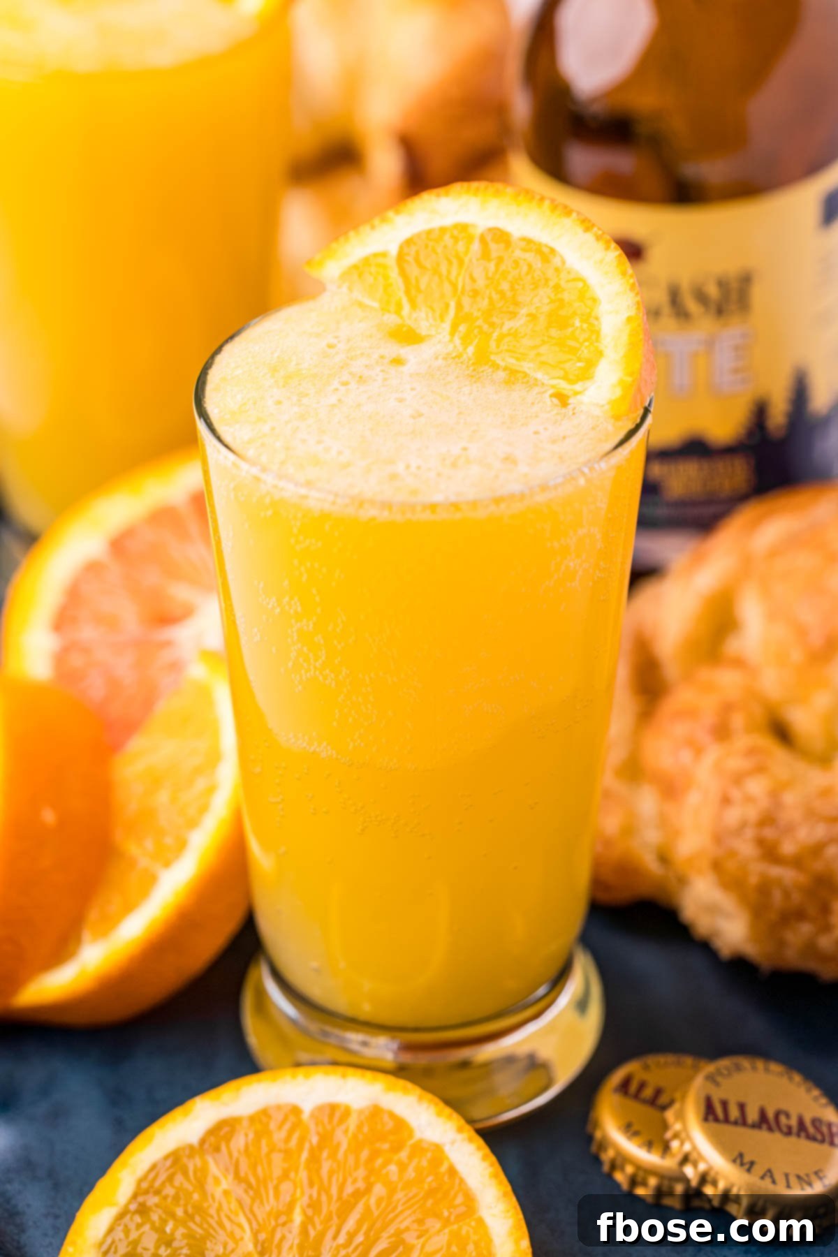 Close up photo of a beermosa on a blue serving platter with croissants and oranges, capturing the brunch ambiance.