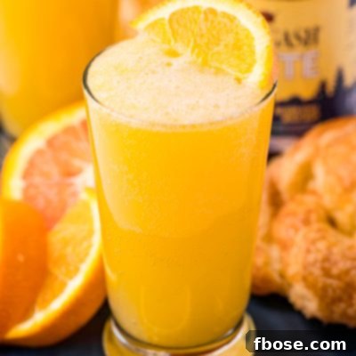 Close up photo of a beermosa on a blue serving platter with croissants and oranges.