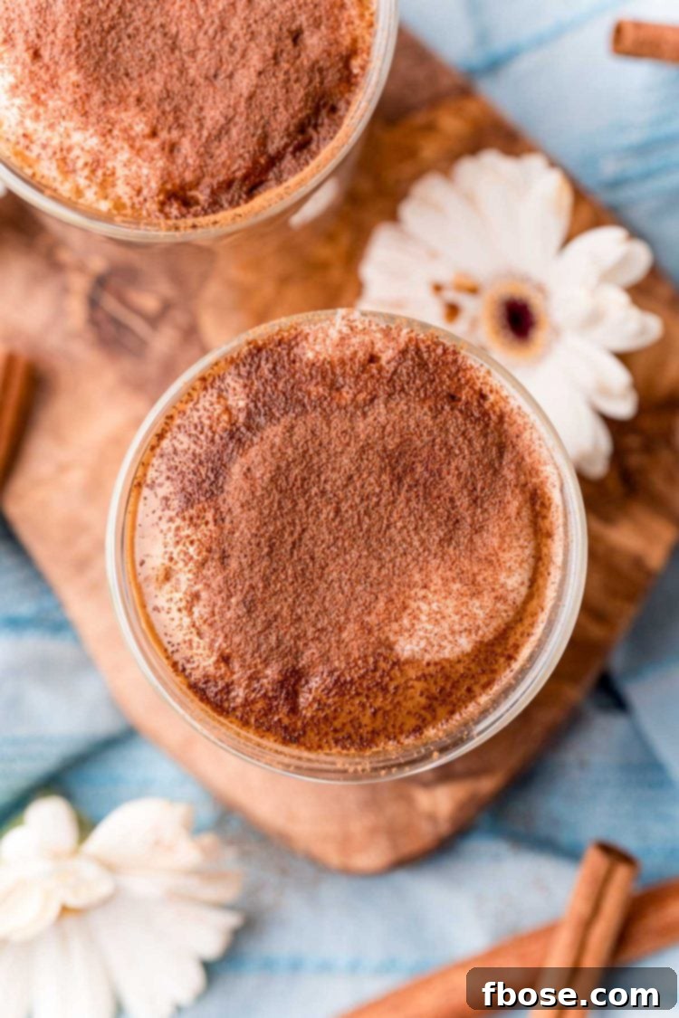 Overhead photo of cafe con miel on a wooden cutting board with cinnamon sticks and flowers around it.