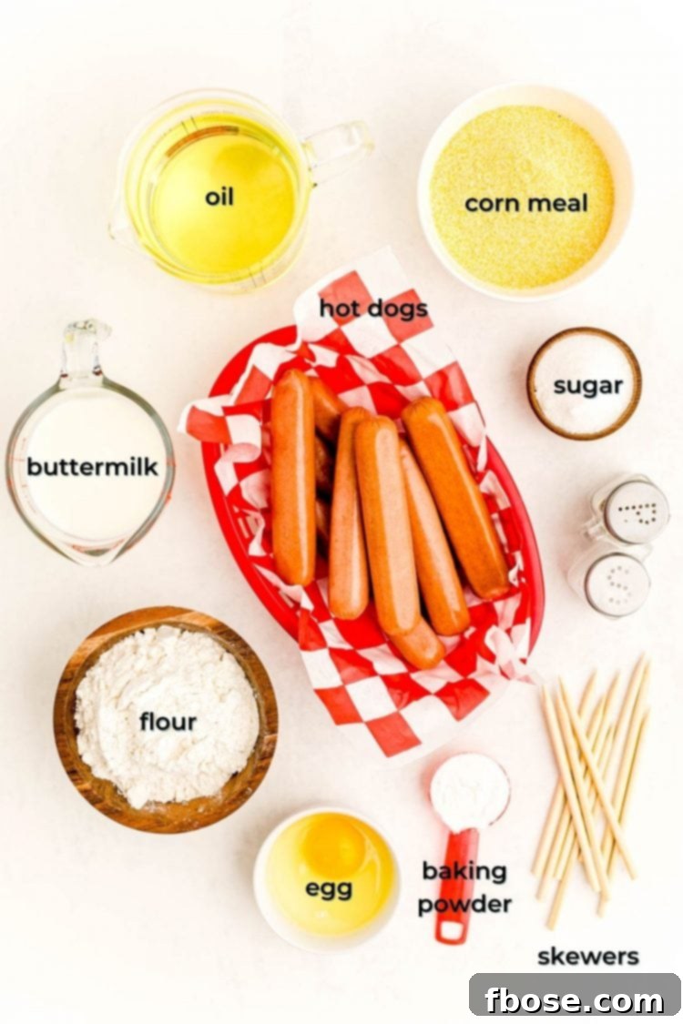 Overhead photo of ingredients prepped to make mini corn dogs with labels including flour, cornmeal, hot dogs, buttermilk, egg, skewers, and oil.