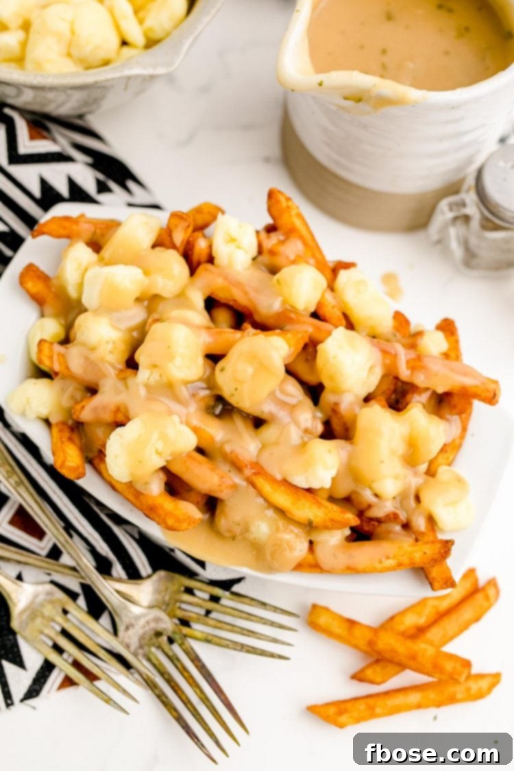 Overhead photo of a paper tray with poutine in it. Pitcher of gravy on the side.