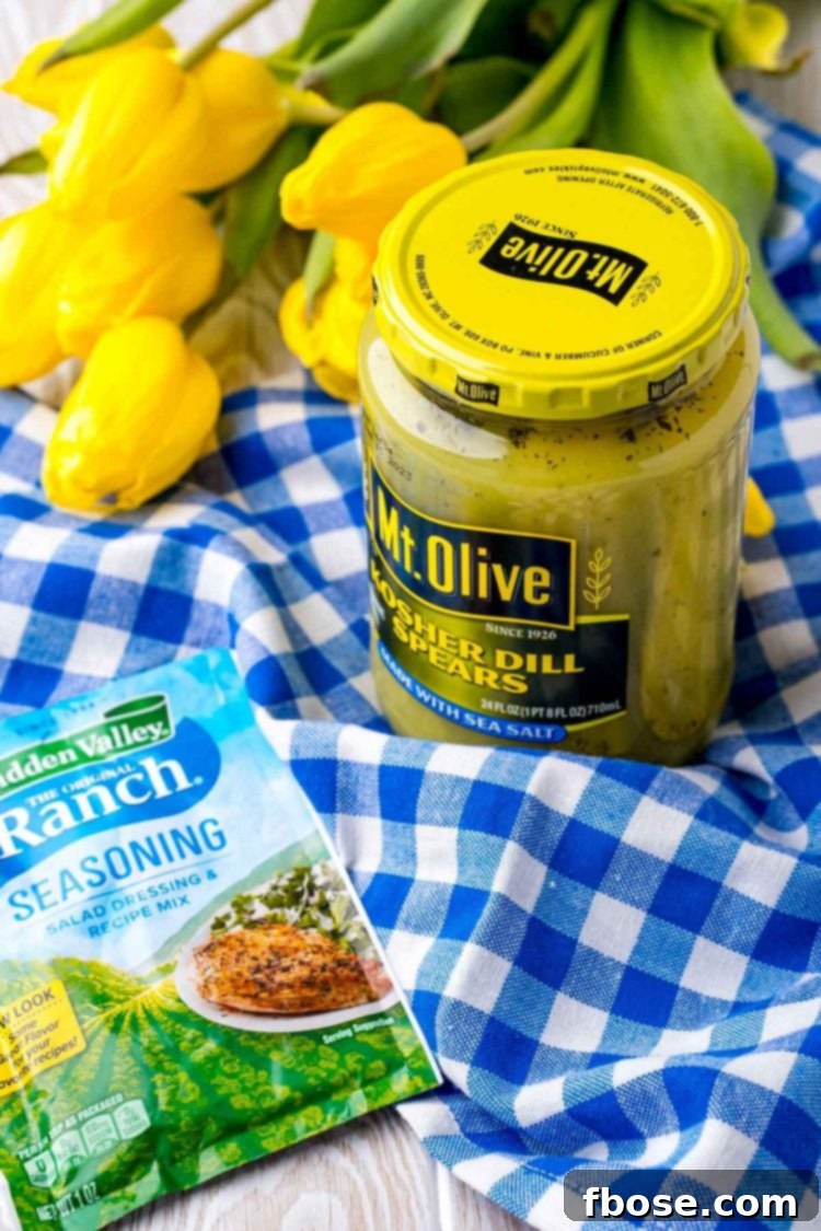 A packet of ranch seasoning resting beside a jar of dill pickles on a rustic blue and white gingham napkin.