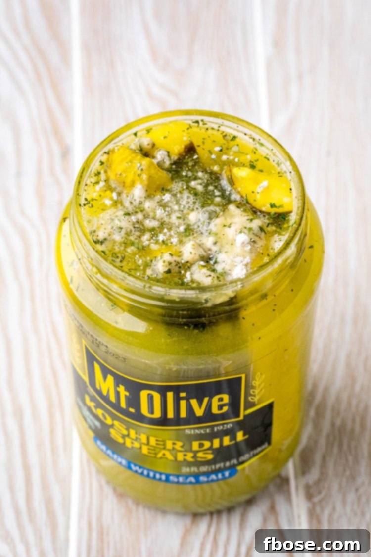 Close up photo of a jar of dill pickles with ranch seasoning visibly mixed into the brine.