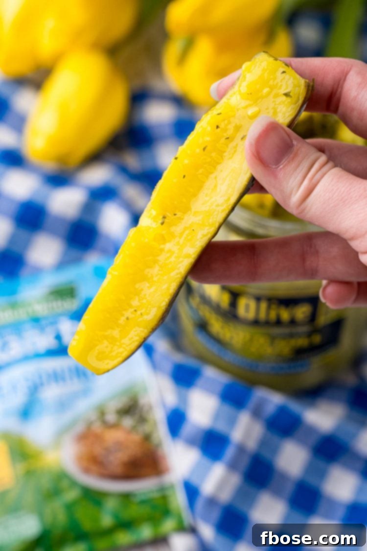 Close up photo of a woman's hand holding a single ranch pickle spear up to the camera, inviting a bite.