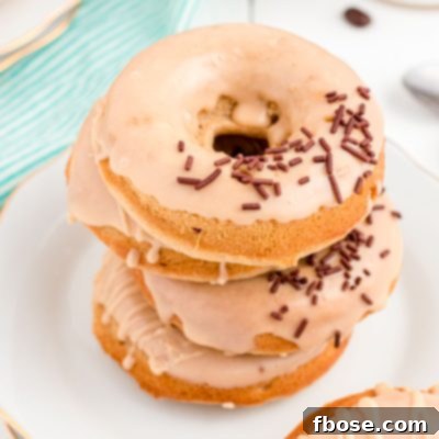 Close up photo of coffee donuts stacked on top of each other on a white plate.