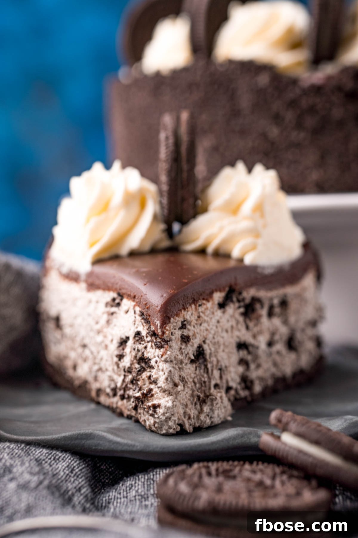 Oreo No-Bake Cheesecake Delight 6 Straight-on view of a single slice of no-bake Oreo cheesecake on a grey plate, with whole Oreos scattered around.