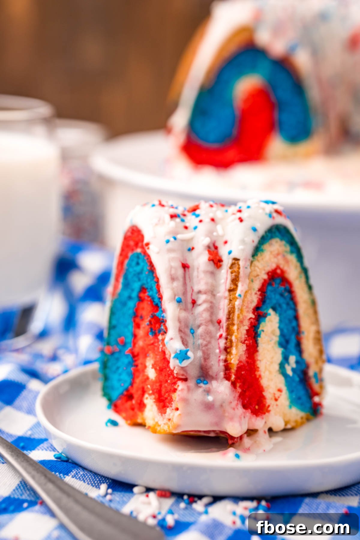 Close up photo of a slice of 4th of july bundt cake on a white plate on a blue gingham napkin, ready to be enjoyed.