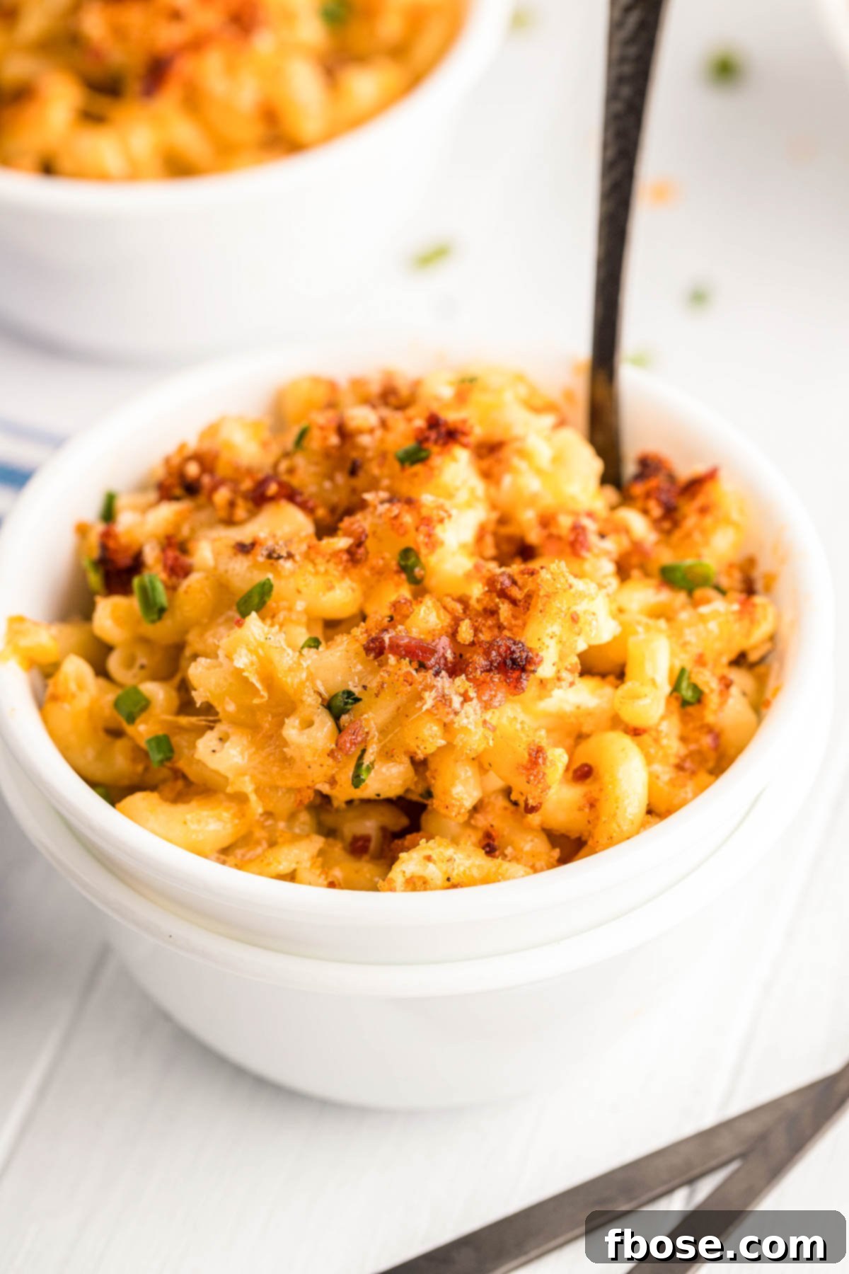 Close up photo of smoked mac and cheese in a white bowl with a fork in it, showing the gooey cheese pull.