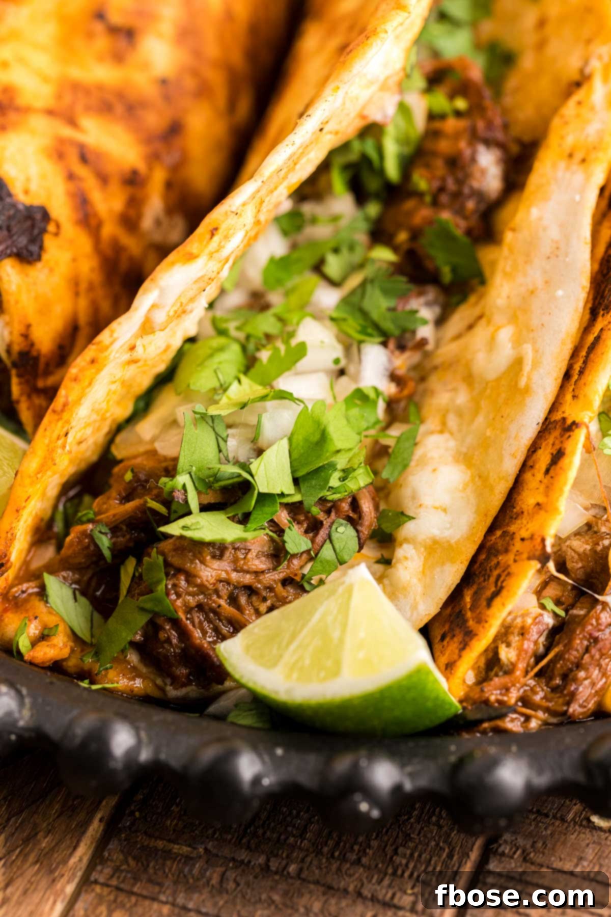 Close up of a birria taco on a black plate with more tacos.