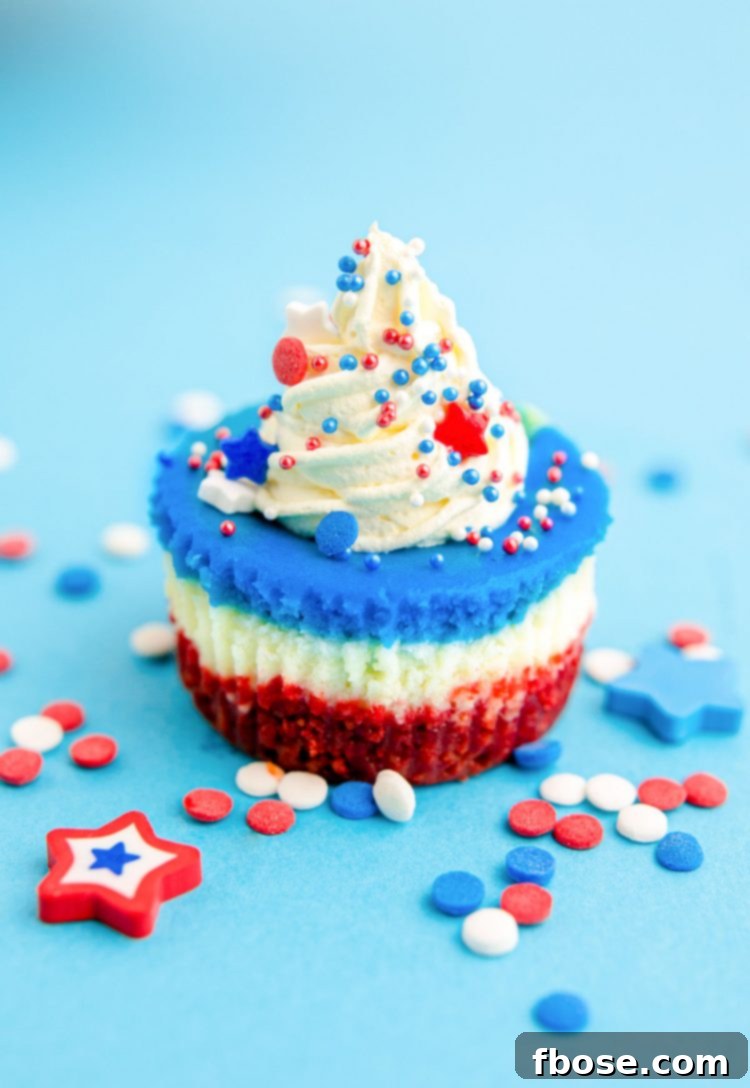 Red White & Blue Mini Cheesecakes 3 A red, white, and blue mini cheesecake sitting on a blue surface with sprinkles all around.