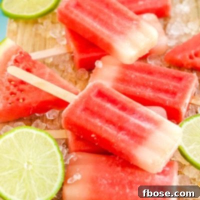 Close up photo of watermelon popsicles on a wooden cutting board with ice and lime slices scattered around them.