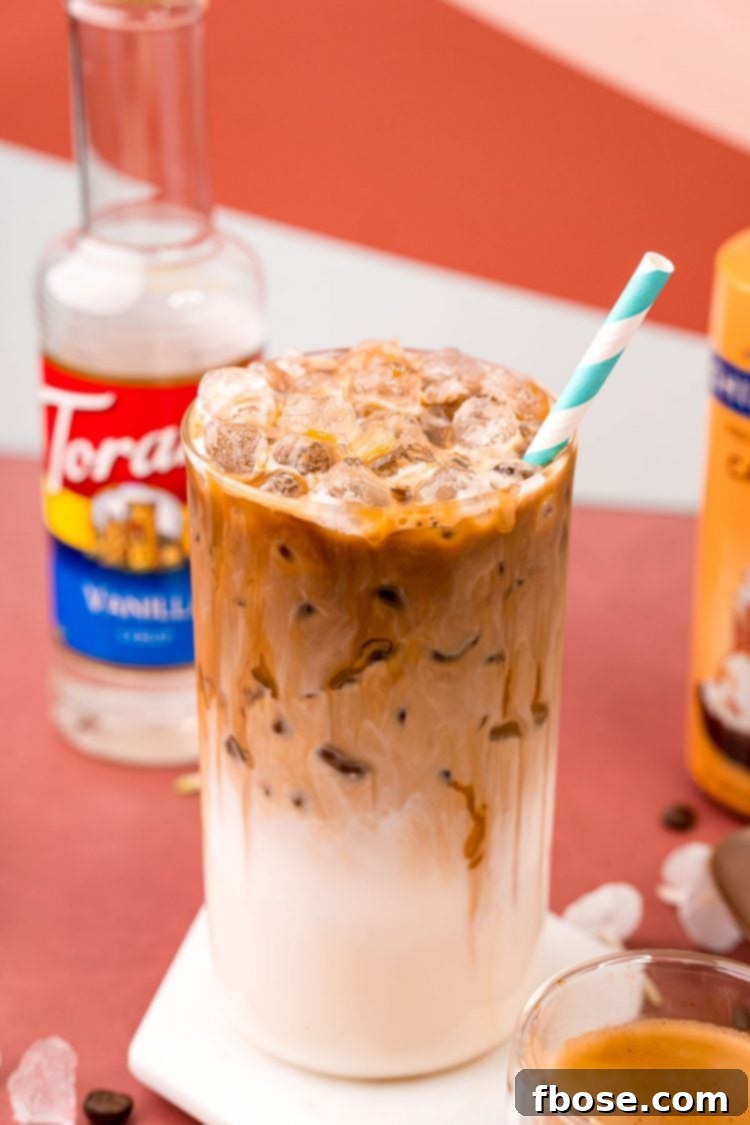 A close up photo of a glass with iced caramel macchiato in it and a bottle of caramel syrup and vanilla simple syrup in the background.