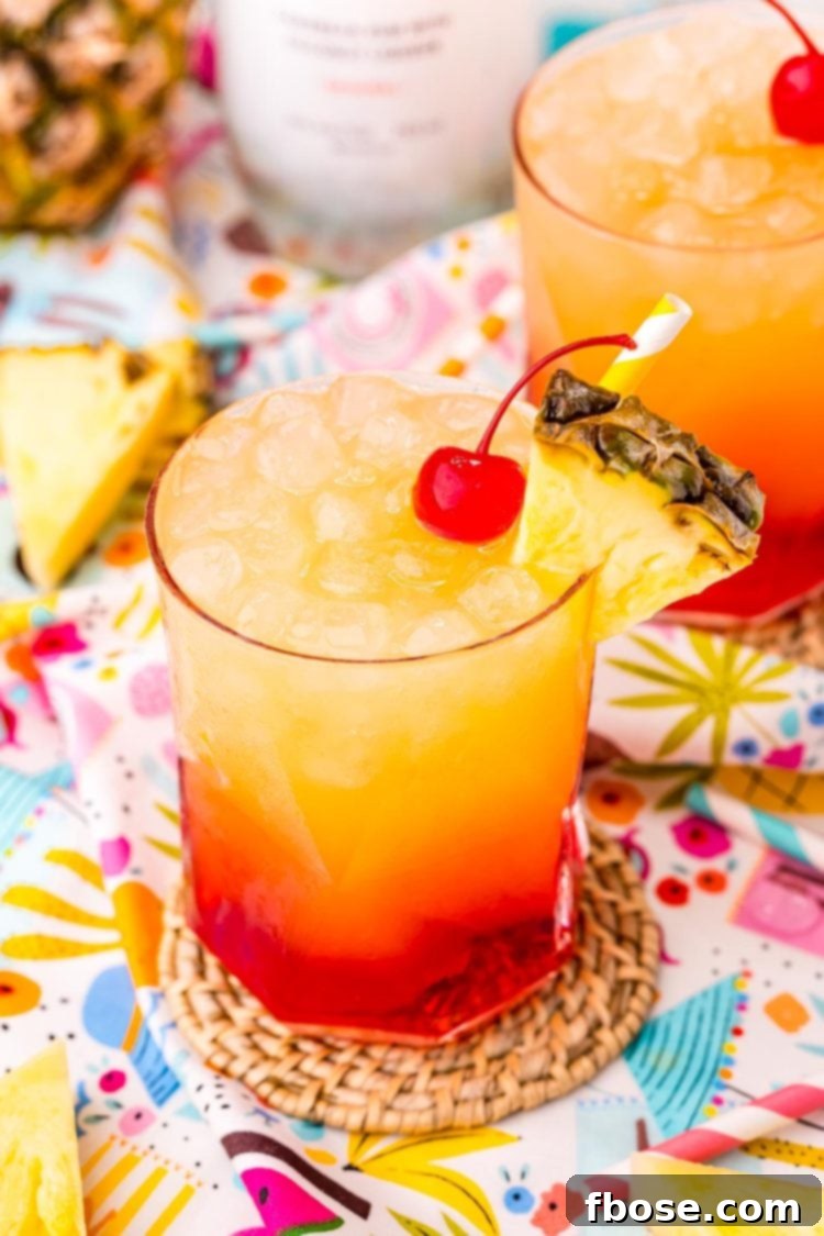 Malibu Sunset 2 Close up photo of a Malibu Sunset drink on a colorful printed napkin with pineapple wedges and another drink in the background.