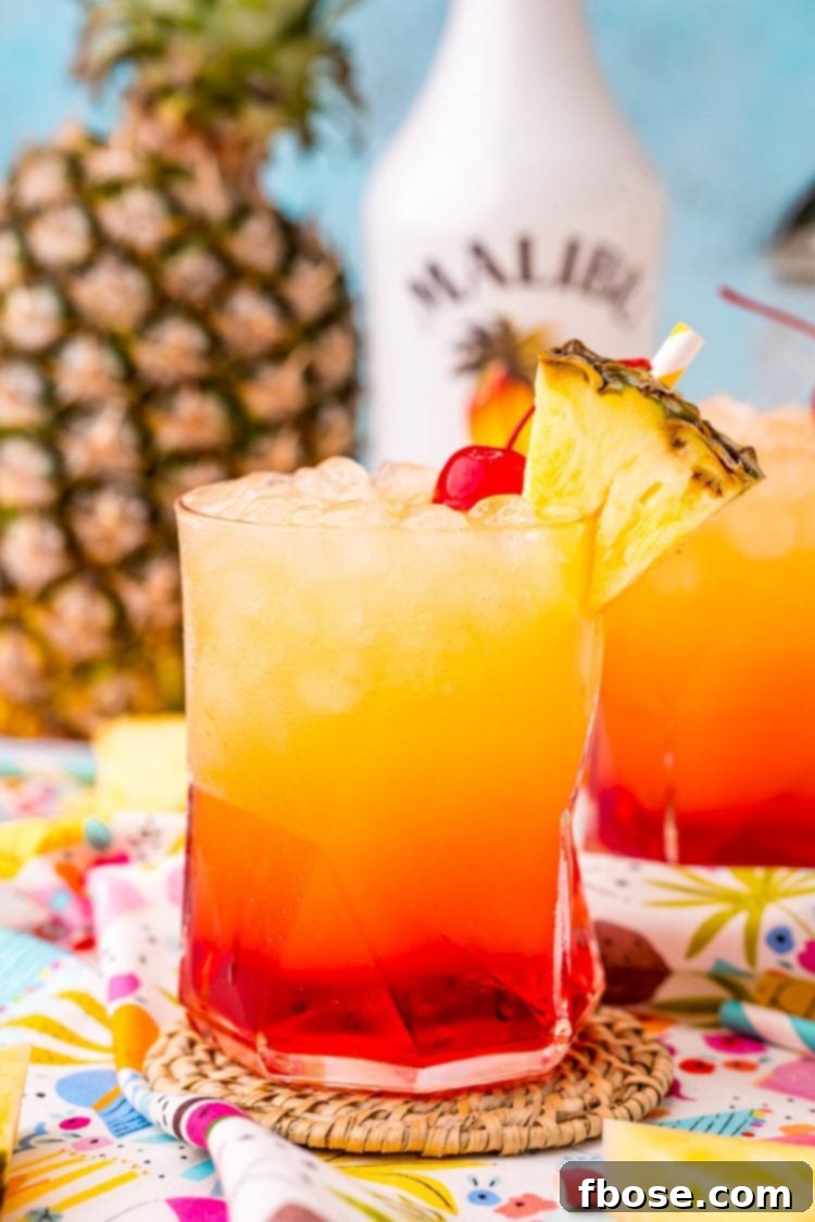 Malibu Sunset 3 Close up photo of a Malibu sunset drink on a colorful napkin with another glass and pineapple in the background.
