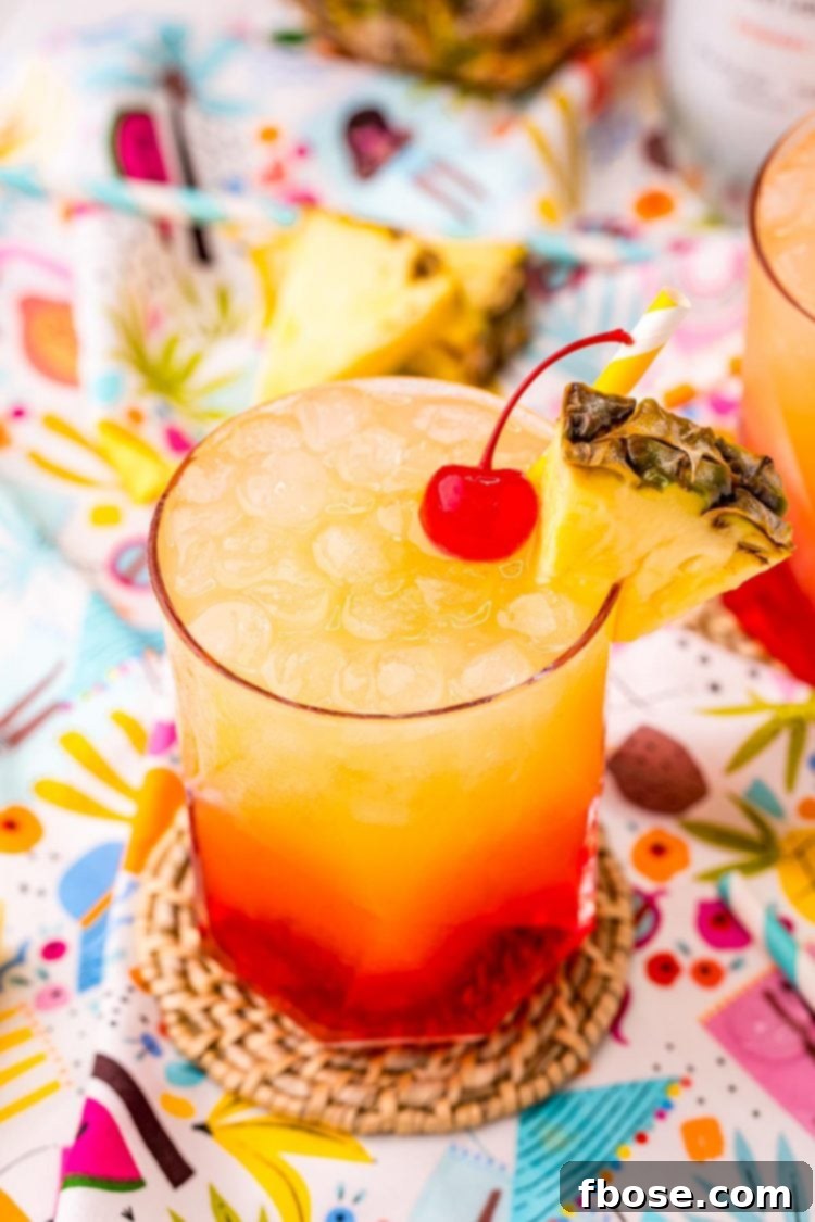 Malibu Sunset 5 Close up photo of a Malibu Sunset drink on a colorful printed napkin with pineapple wedges and another drink in the background.