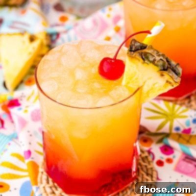 Malibu Sunset 6 Close up photo of a Malibu Sunset drink on a colorful printed napkin with pineapple wedges and another drink in the background.
