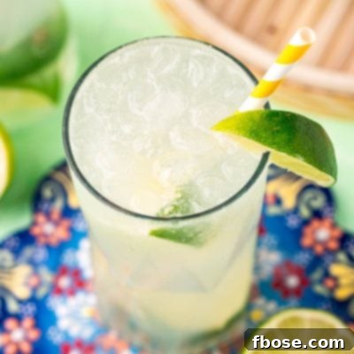 Close up photo of a ranch water cocktail on a colorful trivet with a white and yellow striped paper straw and lime wedges.