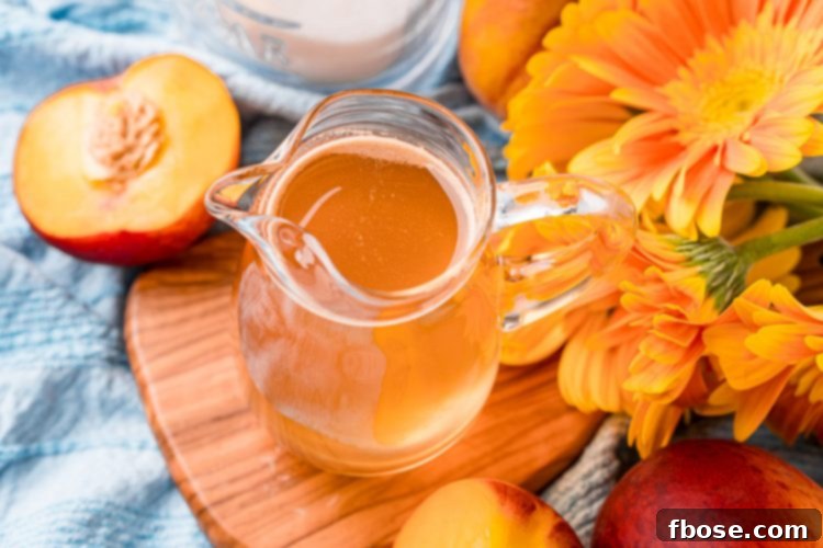 Horizontal photo of a small pitcher of peach simple syrup on a wooden cutting board.