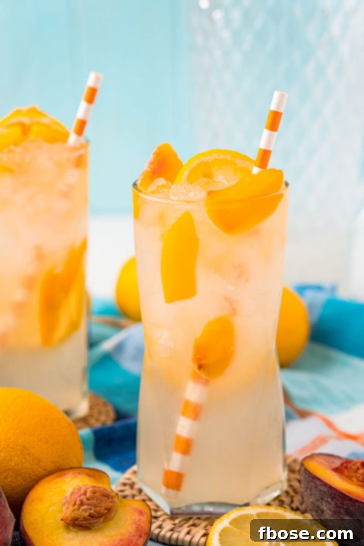 Two glasses of peach lemonade on coasted on a table with peaches scattered around.