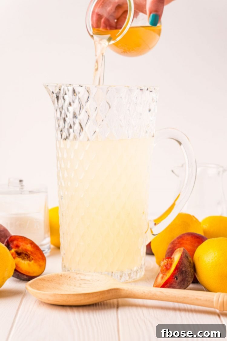 Photo of peach simple syrup being poured into a large pitcher to make lemonade.